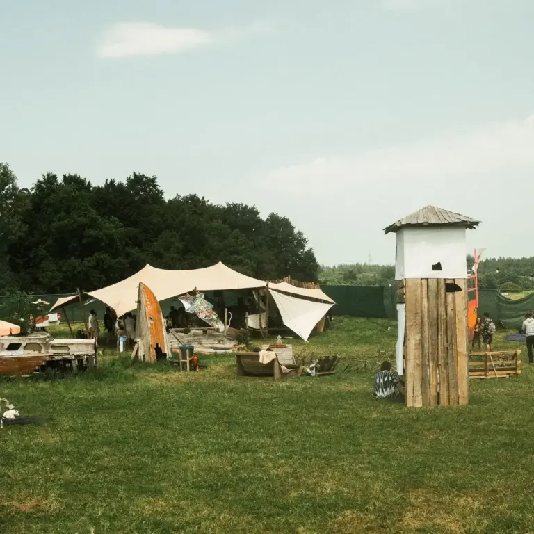 Weitläufiges Festivalgelände des DachüberKopf mit Chill-Area, Sonnensegeln, Holzbooten und einem markanten Holzwachturm im Hintergrund